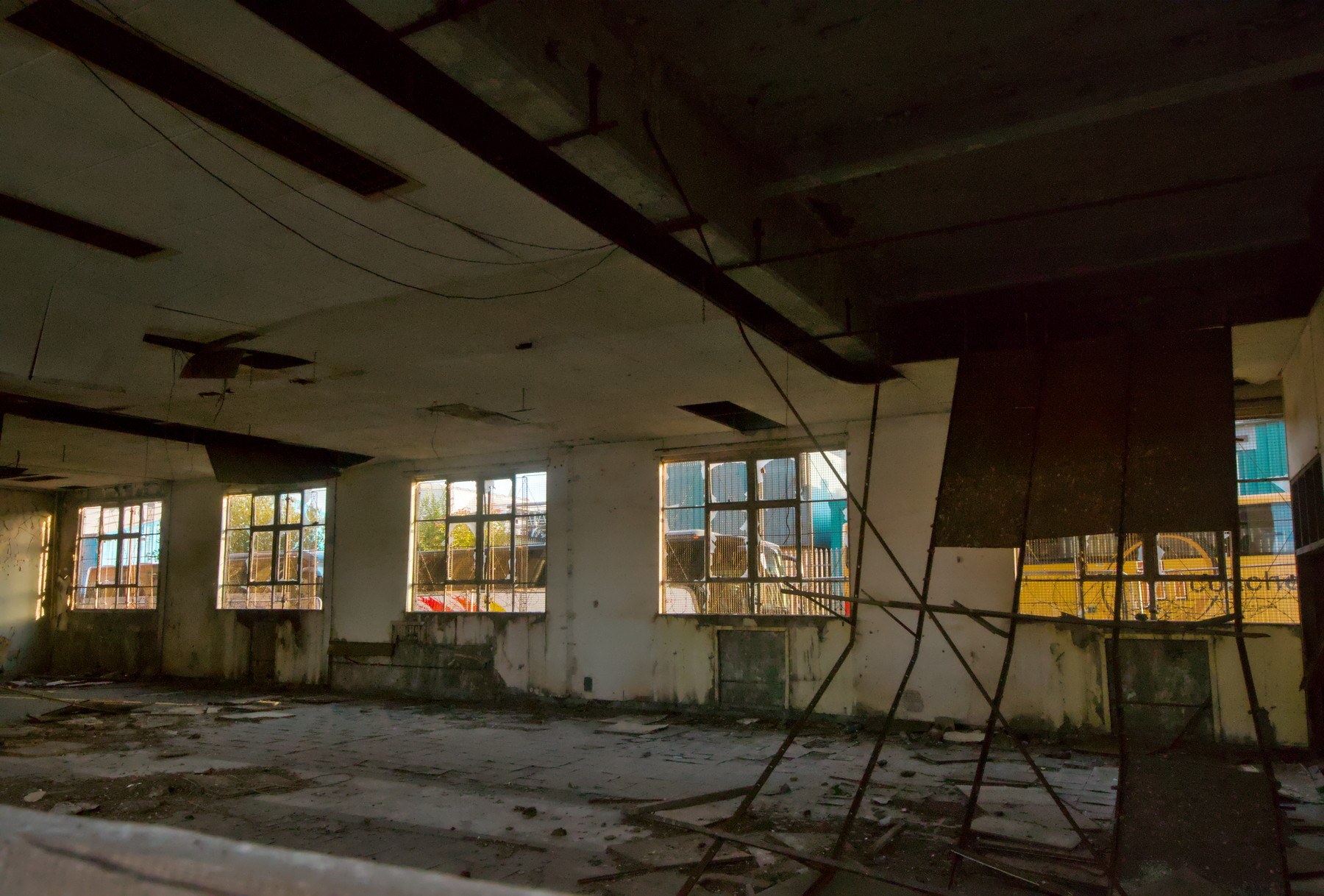 Dim, derelict interior at Sentinel Works, with debris on the concrete floor, hanging cables, broken ceiling panels and rows of industrial windows.