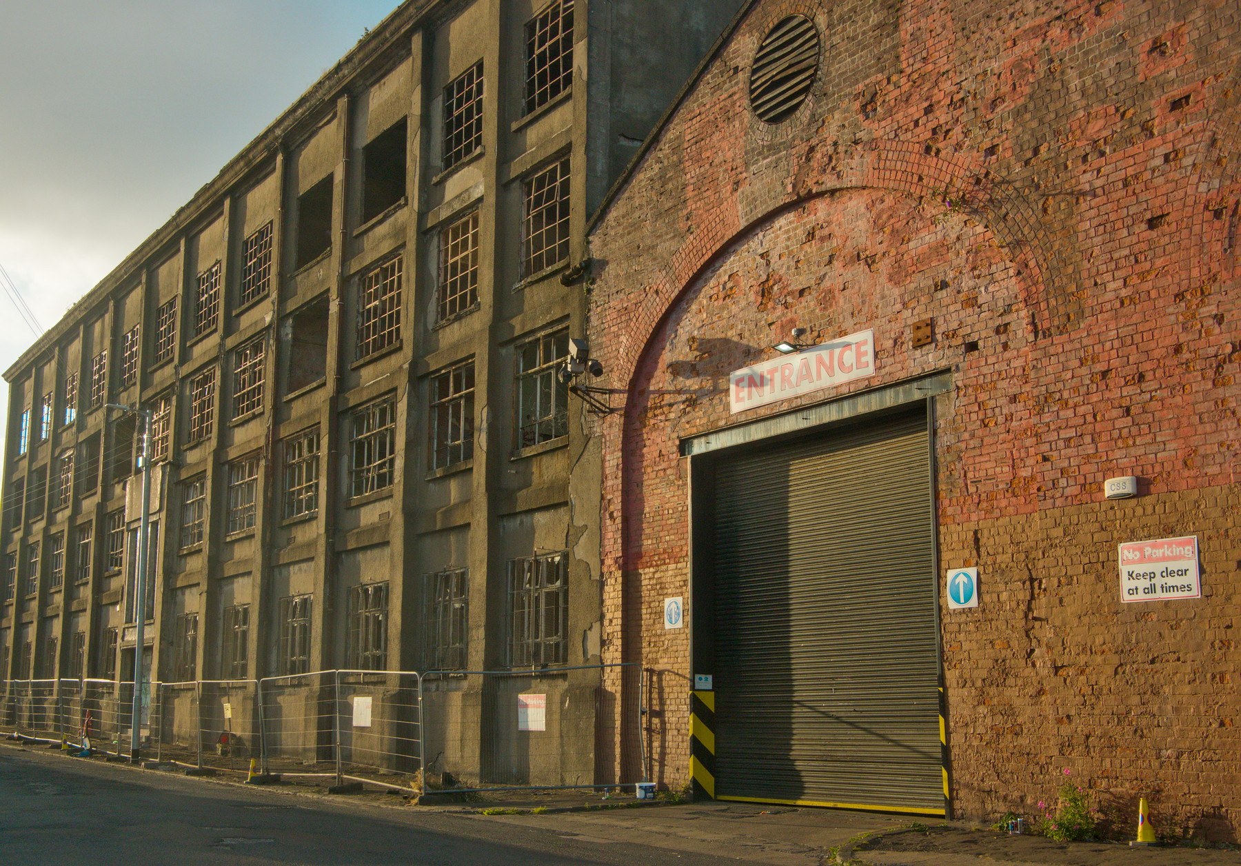 Weathered brick and concrete industrial building at Sentinel Works, with rows of broken-pane windows and a shuttered entrance beneath a faded sign.