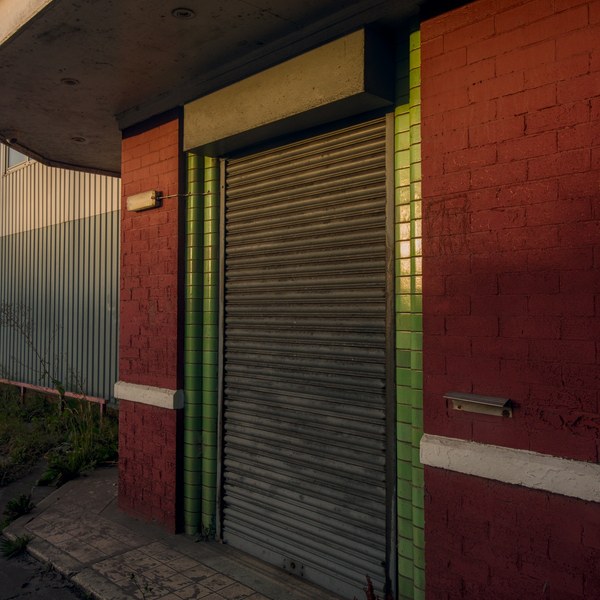 Closed metal roller shutter set in a red-brick industrial building, framed by glossy green tiles beneath a weathered concrete canopy.
