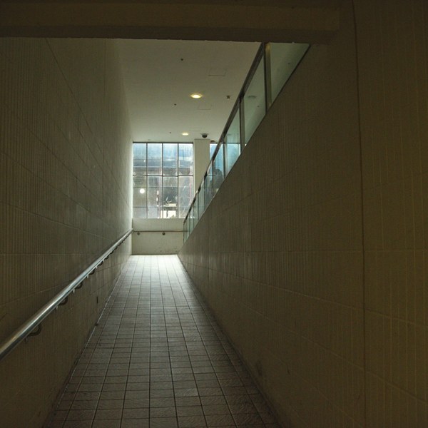 Tiled interior ramp with a metal handrail on the left, rising toward large windows and daylight at Cumbernauld Center.
