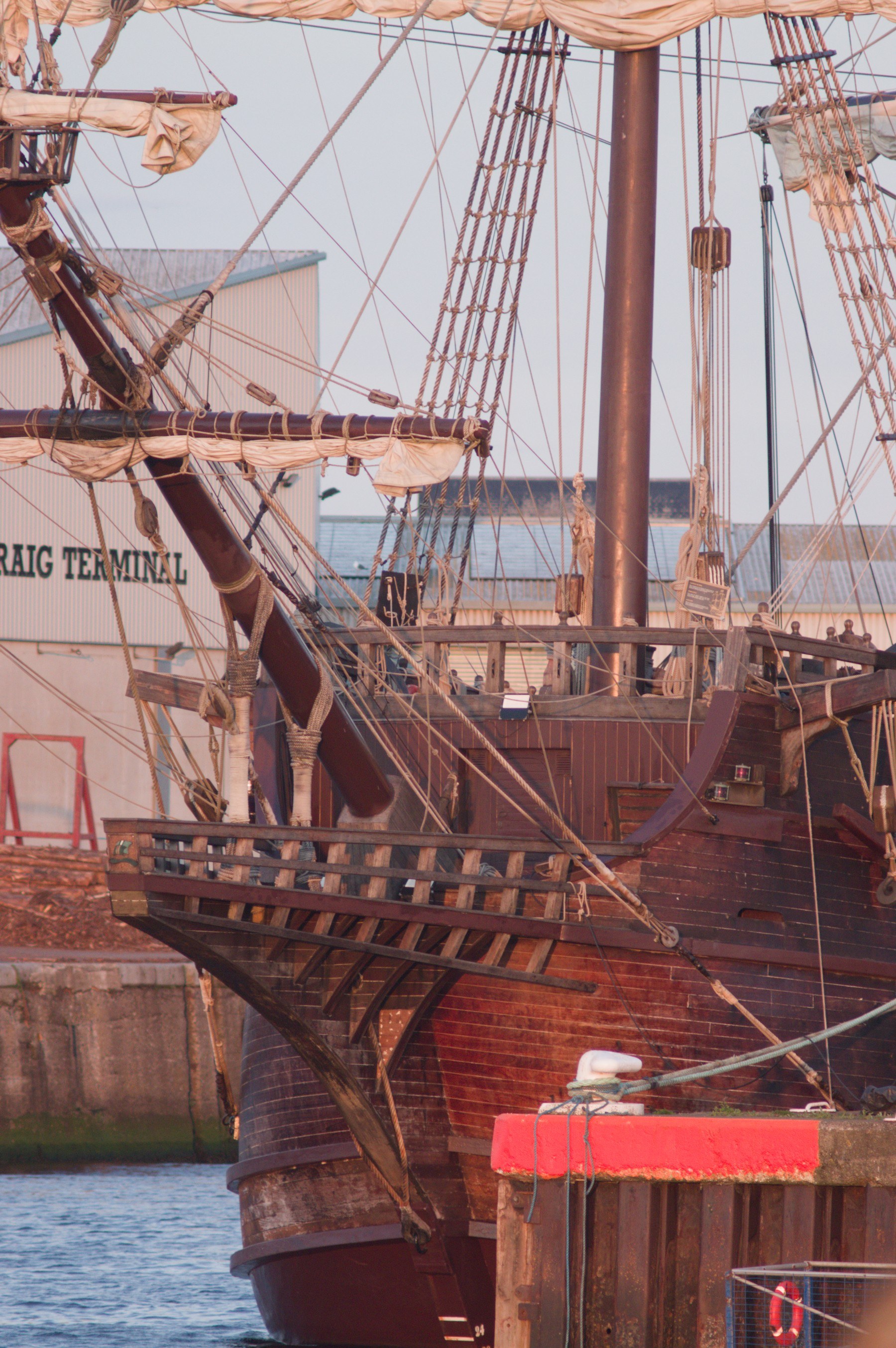 Close view of Galeón Andalucía’s wooden bow alongside a quay at the Port of Ayr, with furled sails, dense rope rigging and mooring lines above the water.
