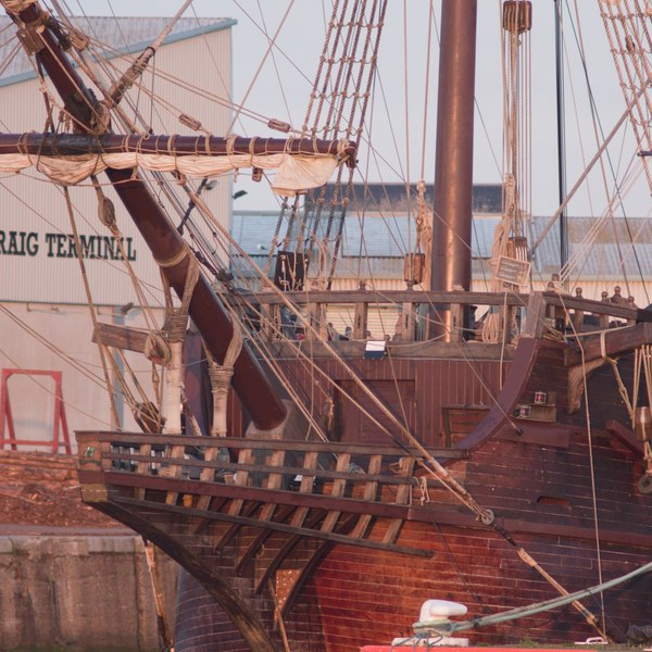 Close view of Galeón Andalucía’s wooden bow alongside a quay at the Port of Ayr, with furled sails, dense rope rigging and mooring lines above the water.