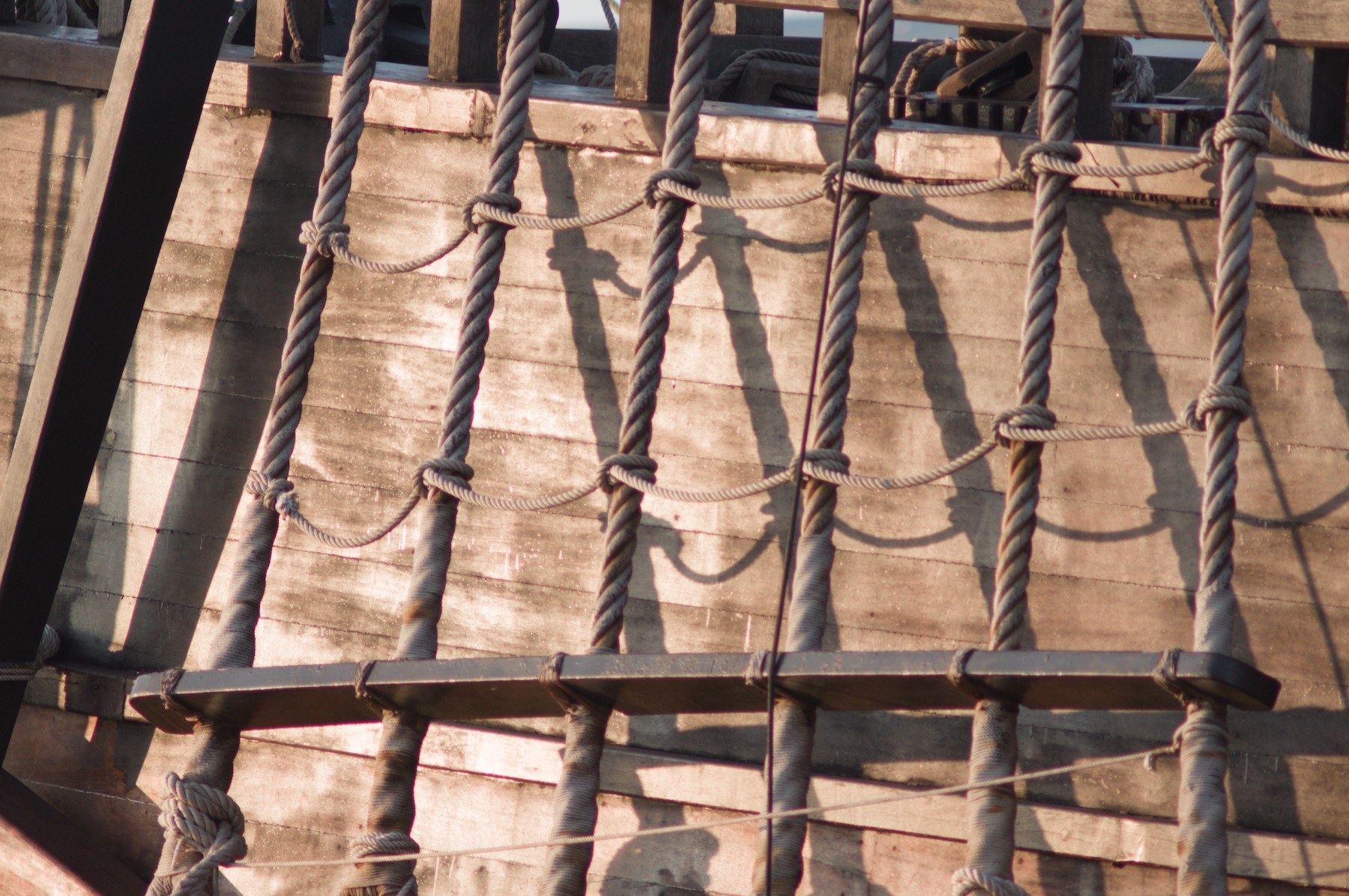 Close-up of knotted rope lines forming a ladder-like grid over sunlit wooden deck planks on Galeón Andalucía.