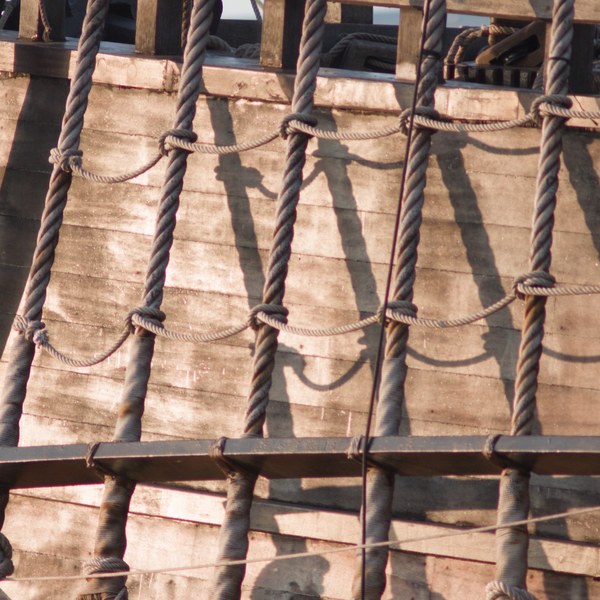 Close-up of knotted rope lines forming a ladder-like grid over sunlit wooden deck planks on Galeón Andalucía.