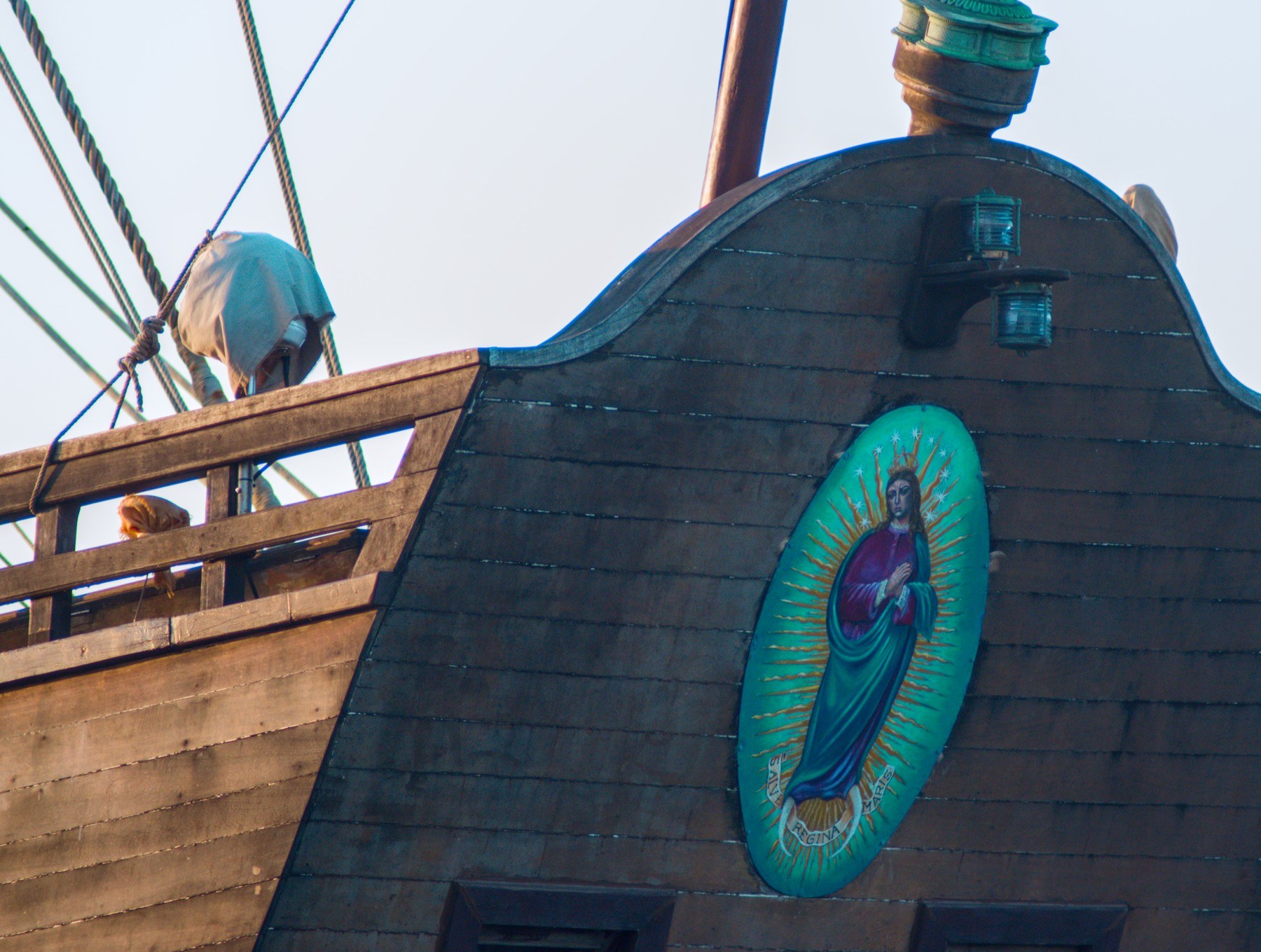 Close view of Galeón Andalucía’s dark wooden side with a turquoise oval devotional image, two small lamps, rope lines and a covered deck fitting.