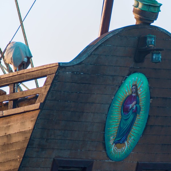 Close view of Galeón Andalucía’s dark wooden side with a turquoise oval devotional image, two small lamps, rope lines and a covered deck fitting.