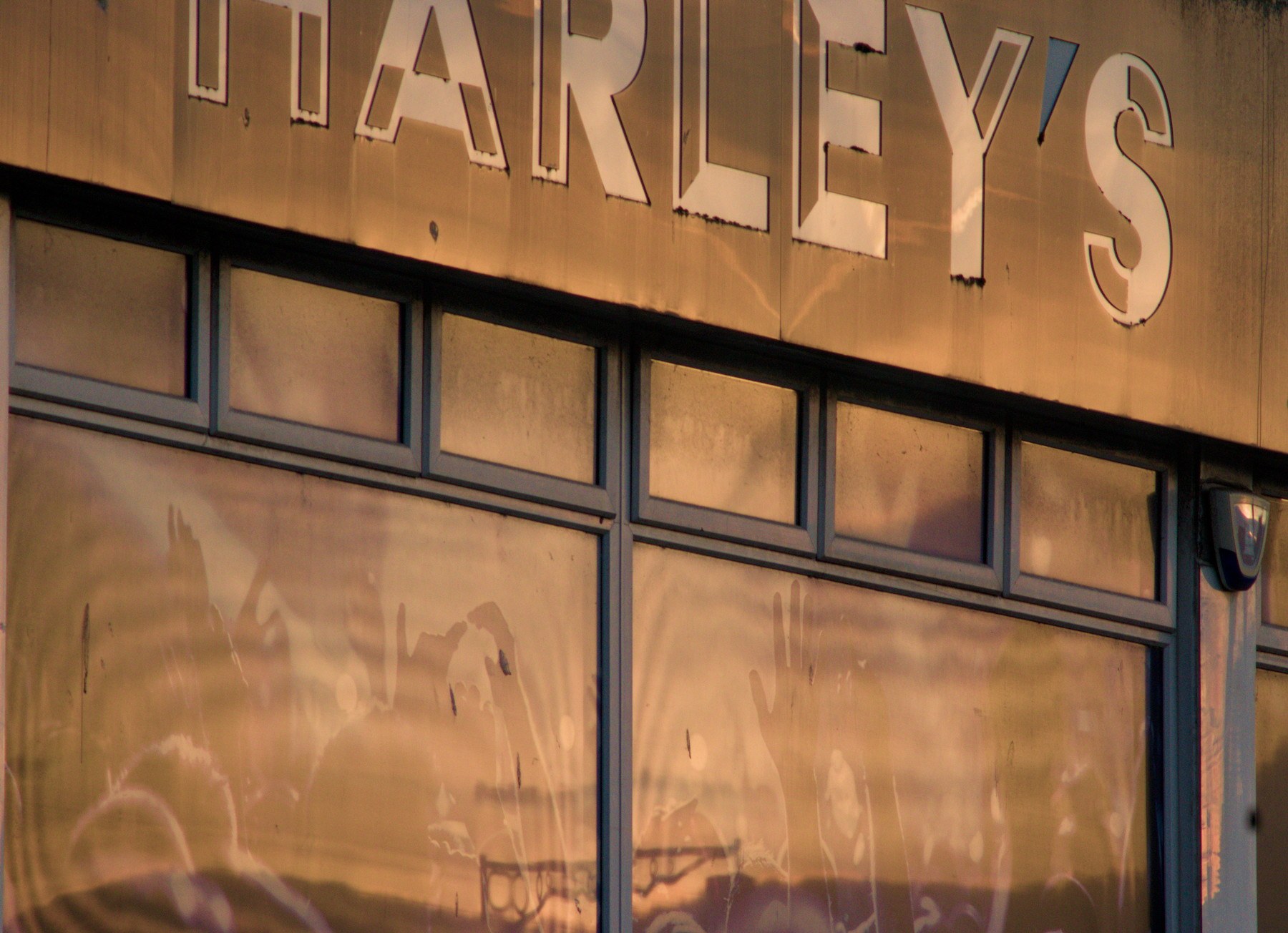 Close view of Harley’s storefront sign above large windows reflecting warm evening clouds and nearby street details.