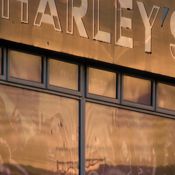 Close view of Harley’s storefront sign above large windows reflecting warm evening clouds and nearby street details.