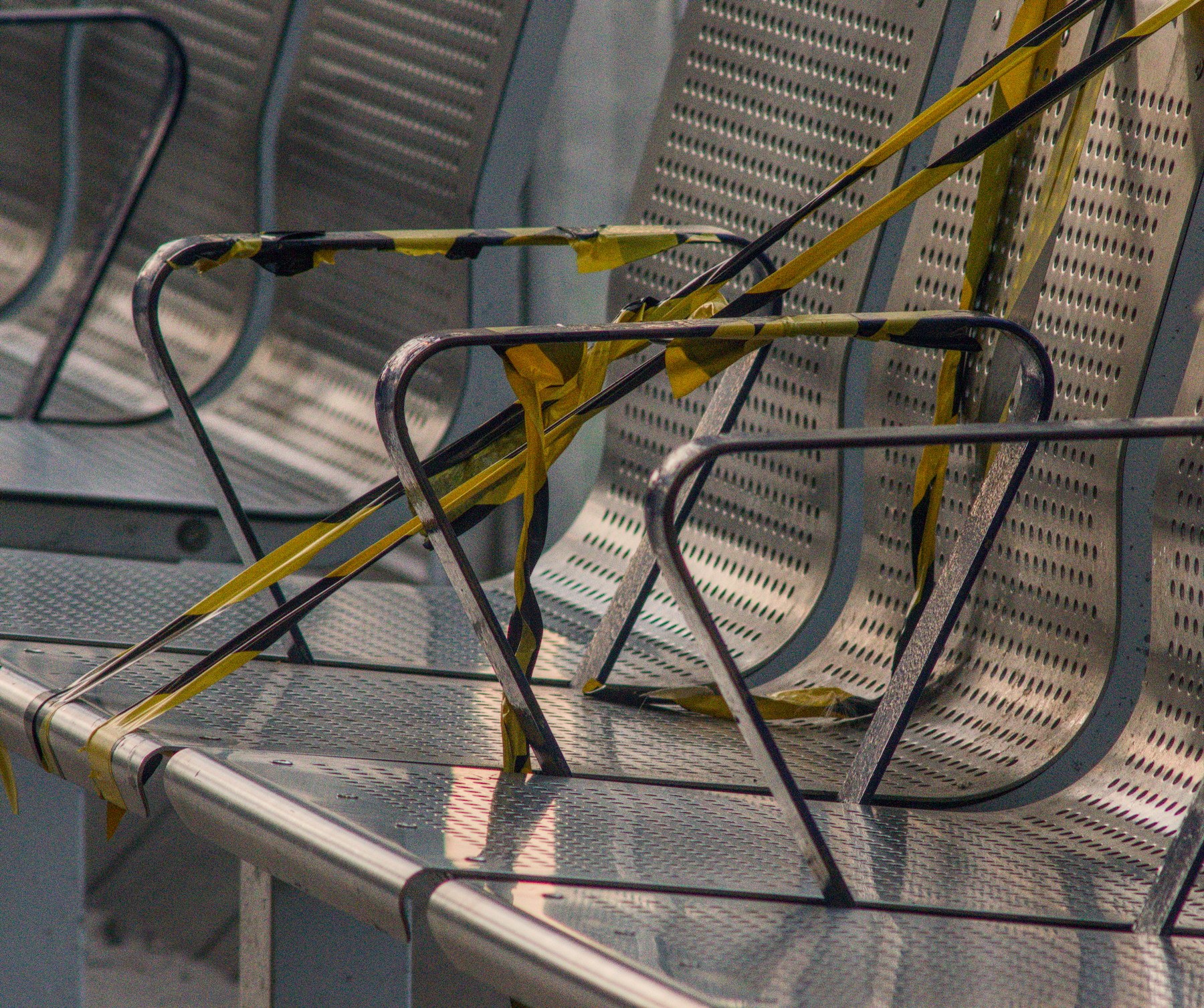 Metal perforated seats with armrests are cordoned off by black-and-yellow tape in evening light.