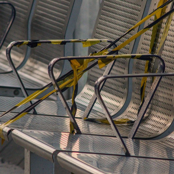 Metal perforated seats with armrests are cordoned off by black-and-yellow tape in evening light.
