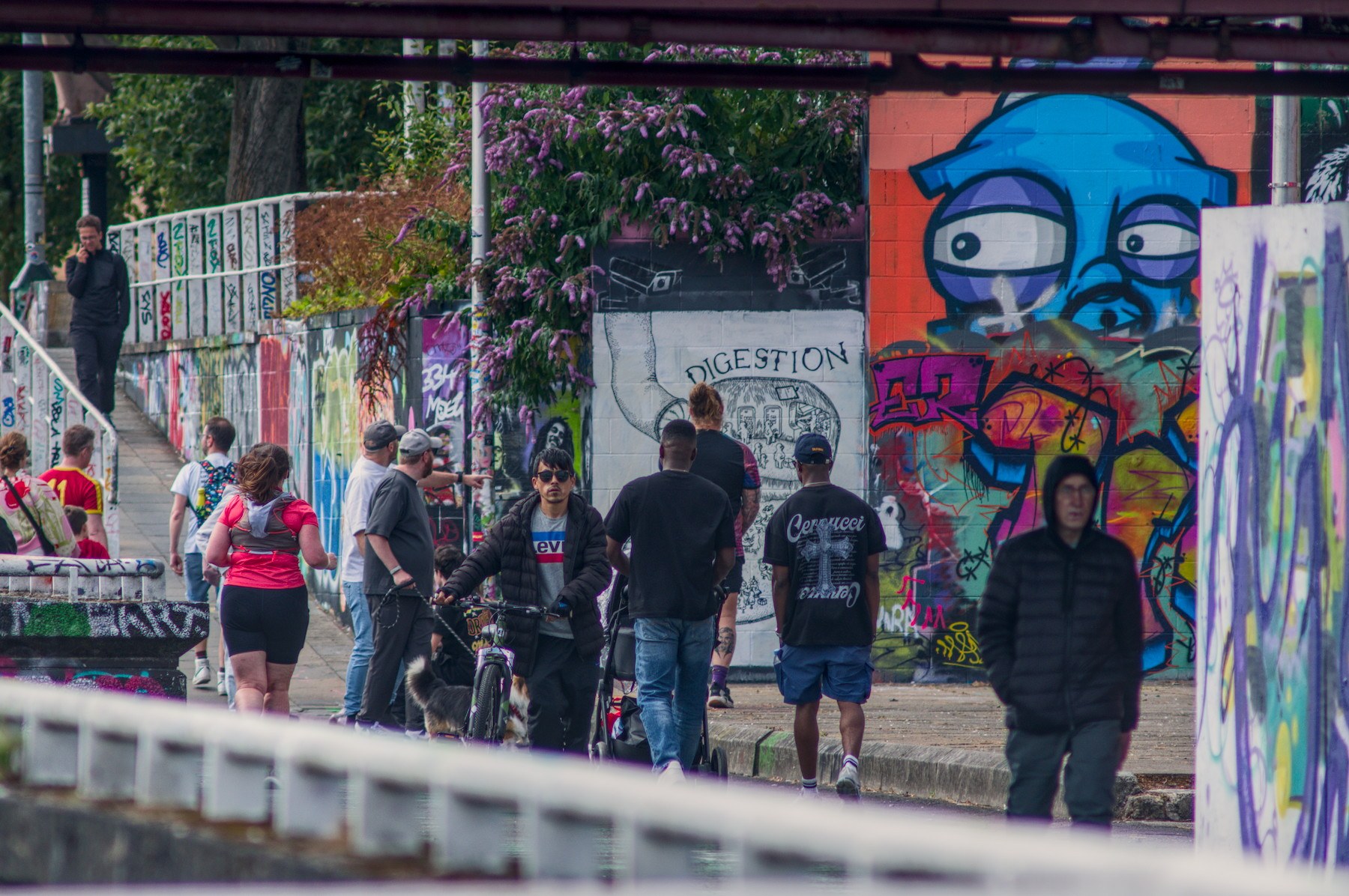 Pedestrians and a cyclist pass colourful graffiti-covered walls beneath a bridge in Glasgow city centre.