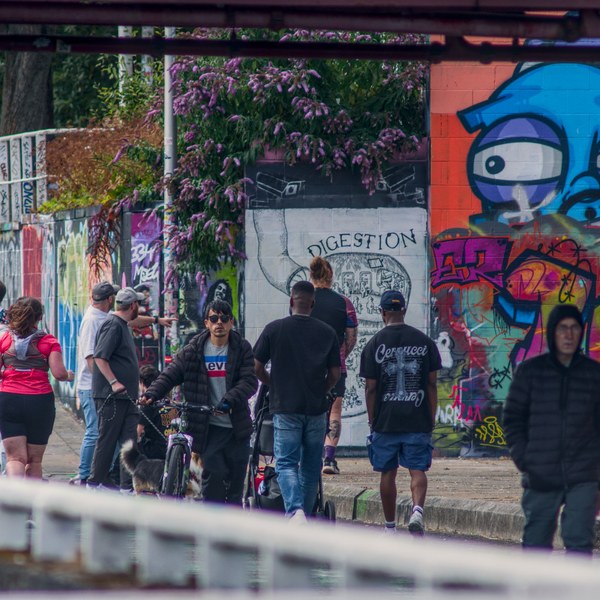 Pedestrians and a cyclist pass colourful graffiti-covered walls beneath a bridge in Glasgow city centre.