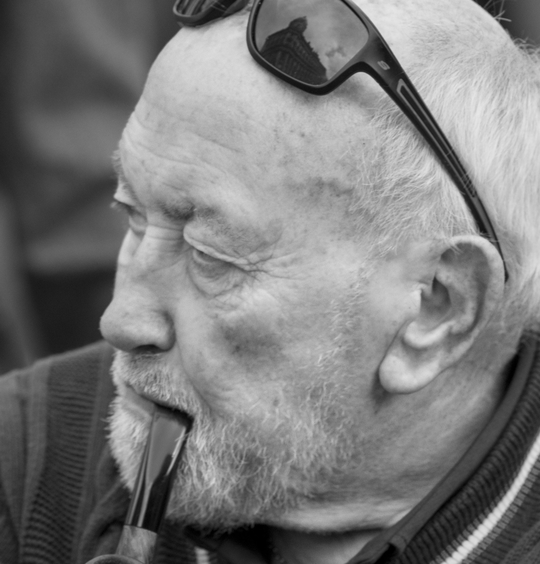 Monochrome close-up portrait of a man in profile, with sunglasses resting on his head and a pipe held in his mouth.