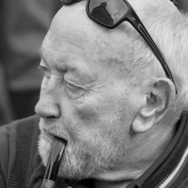 Monochrome close-up portrait of a man in profile, with sunglasses resting on his head and a pipe held in his mouth.