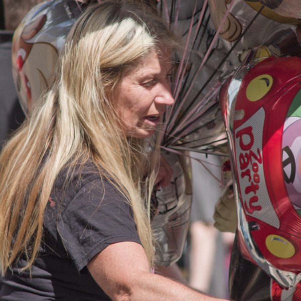Close-up of a blonde woman beside a cluster of shiny helium balloons, including a red cartoon-themed balloon.