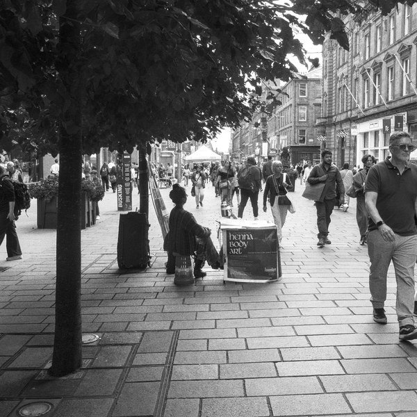 Black-and-white street scene in Glasgow city centre showing pedestrians on a broad paved shopping street, with a man and a boy walking toward the camera beneath a leafy tree.